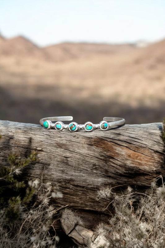 Handcrafted sterling silver cuff with five turquoise stones resting on a weathered log in a desert landscape